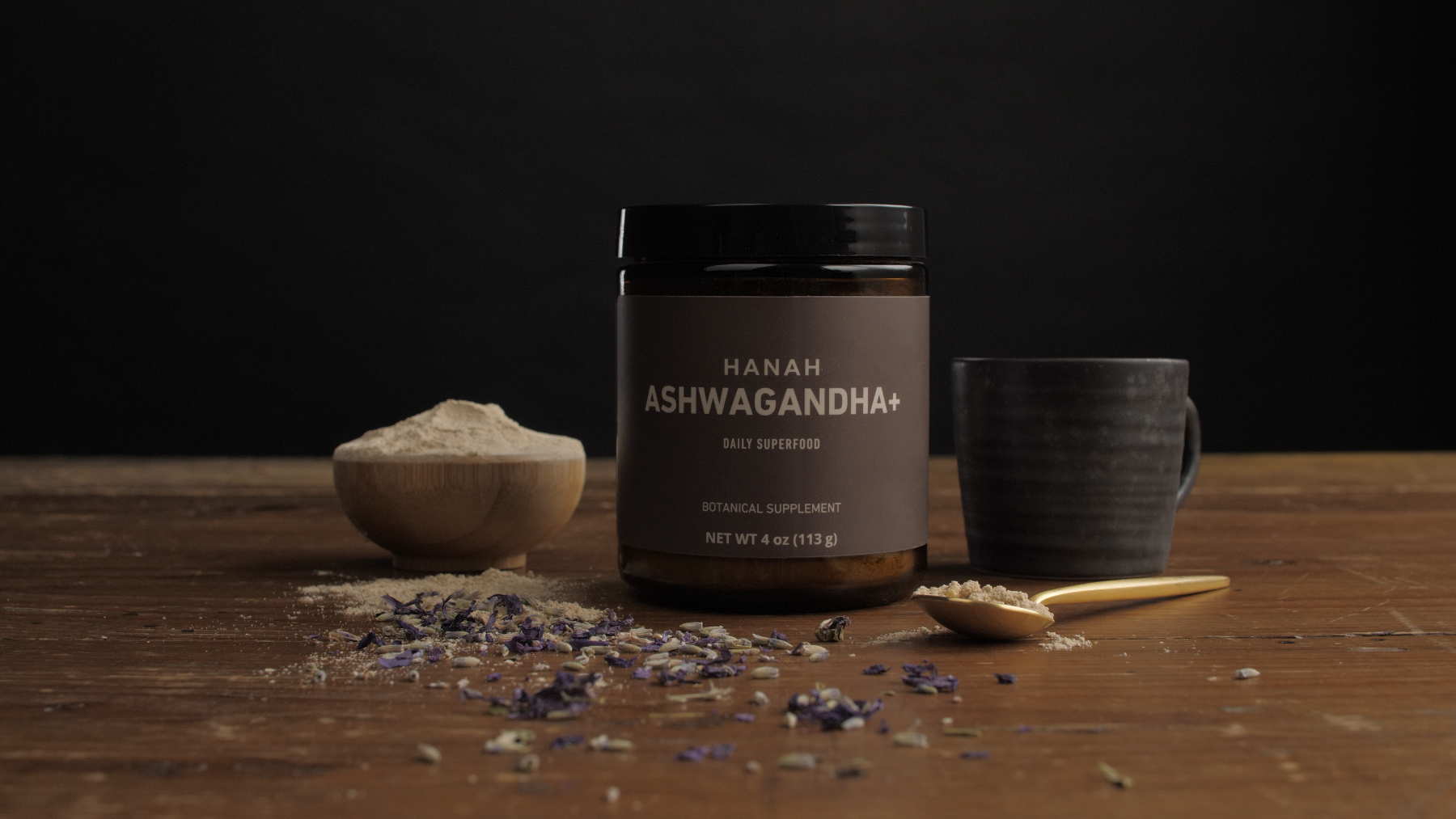 Jar of HANAH Ashwagandha, a daily superfood, surrounded by a wooden bowl, spoon, and mug