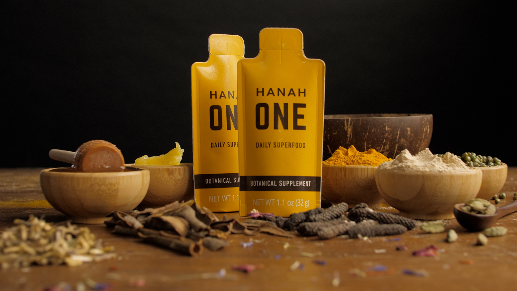Two HANAH ONE Go-Packs, a daily superfood, surrounded by their ingredients in wooden bowls