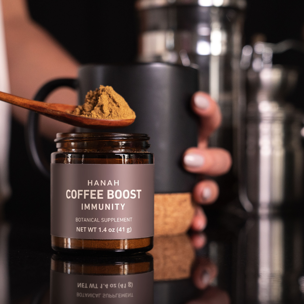 Someone scooping a spoonful of Coffee Boost Immunity from the jar and preparing to add it to a cup of coffee.