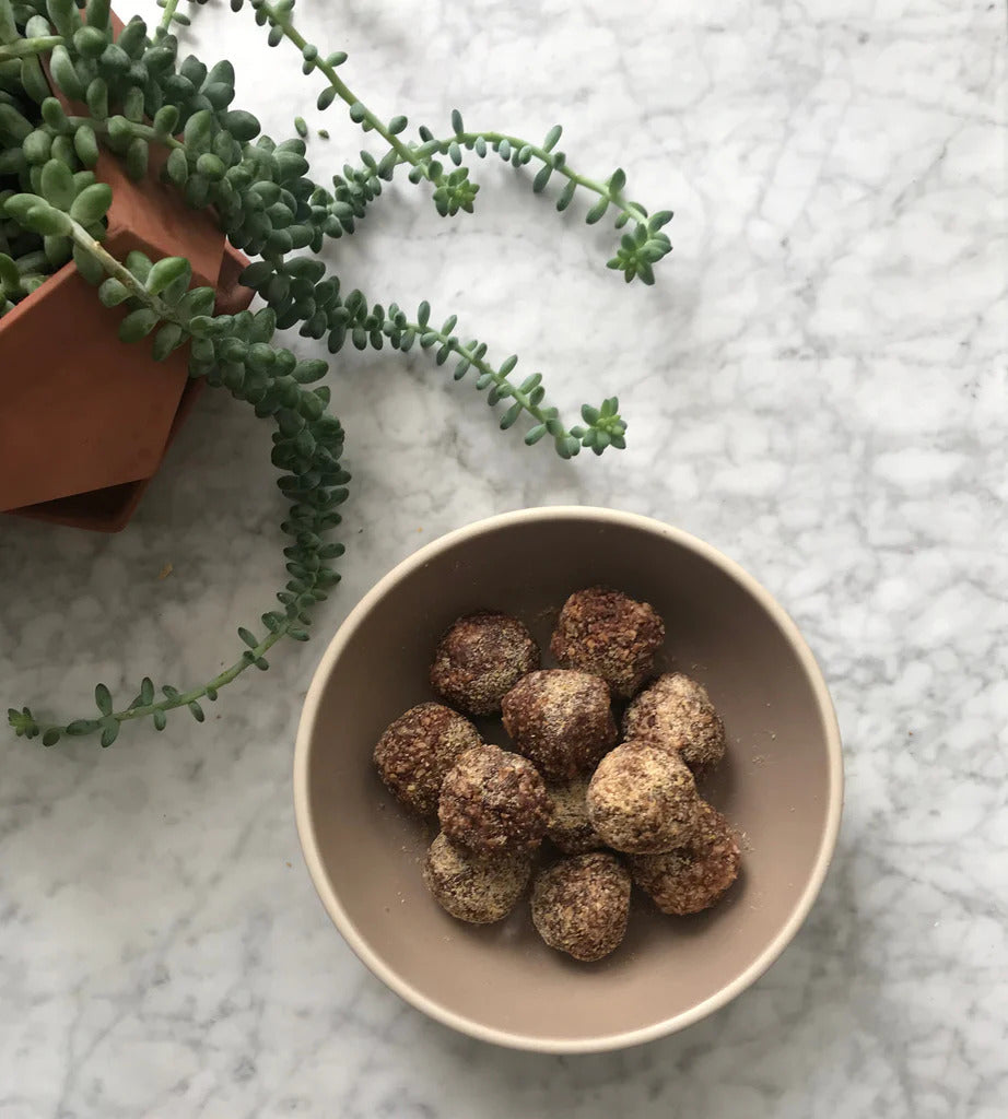 Bowl of raw cacao adaptogen delights infused with HANAH Ashwagandha and HANAH ONE on a marble counter next to a green succulent plant