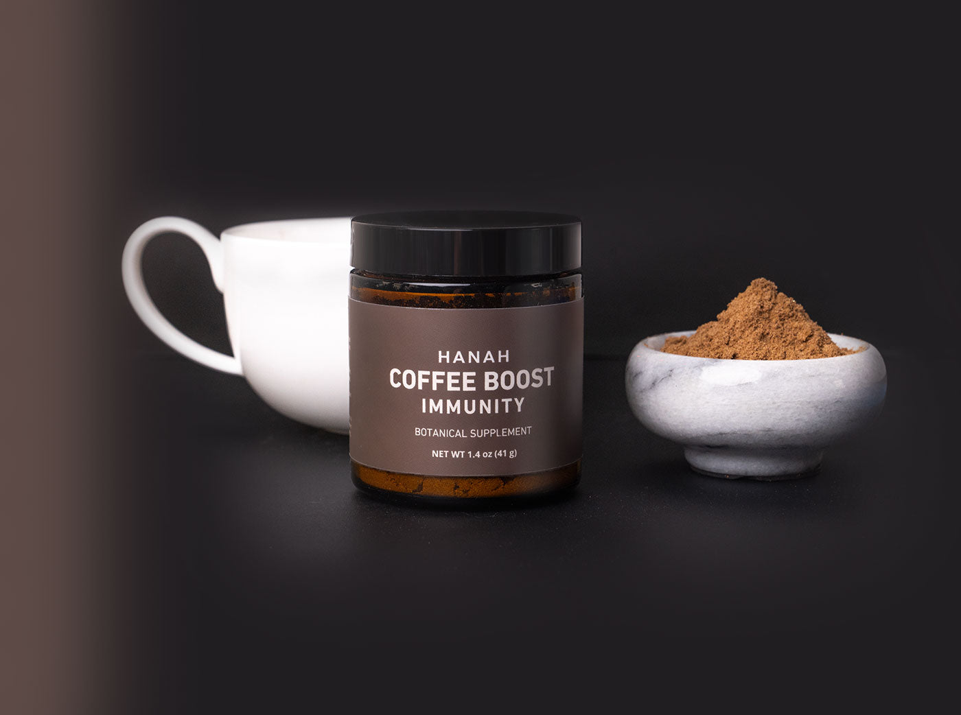 Jar of HANAH Coffee Boost Immunity, a botanical supplement, next to its contents in a marble bowl and cup
